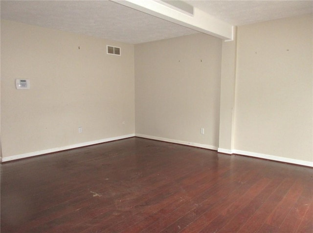 unfurnished room featuring beam ceiling, dark hardwood / wood-style flooring, and a textured ceiling