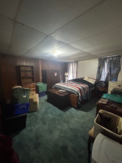 bedroom with a drop ceiling, carpet floors, and wooden walls