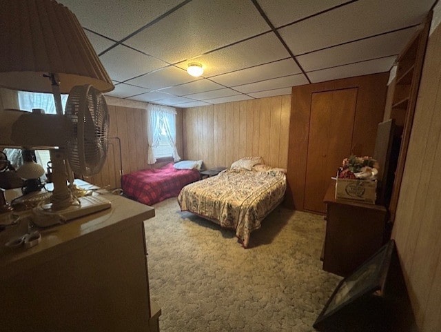 bedroom with carpet, a drop ceiling, and wood walls