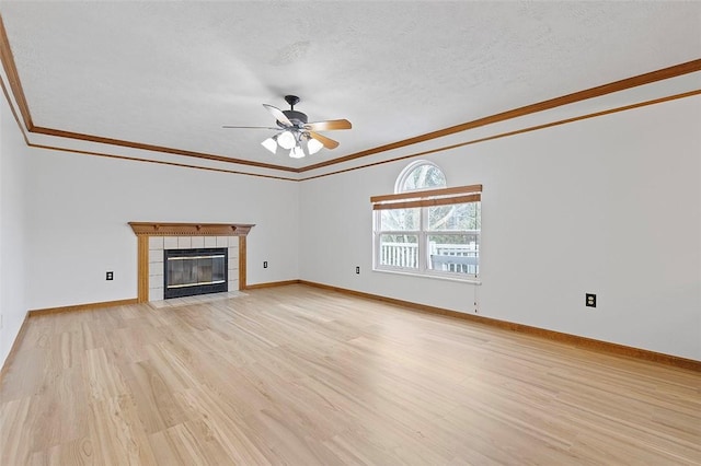 unfurnished living room featuring ceiling fan, light hardwood / wood-style flooring, a textured ceiling, a tiled fireplace, and ornamental molding