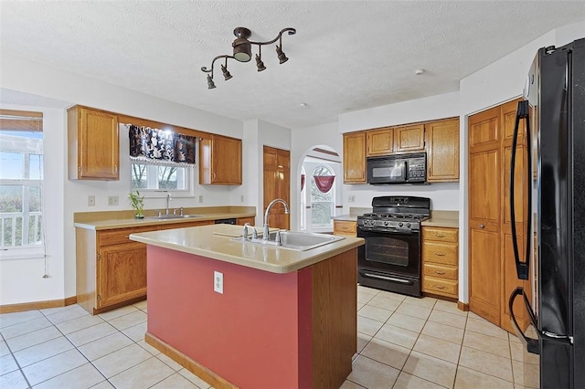 kitchen featuring a kitchen island with sink, sink, light tile patterned flooring, and black appliances