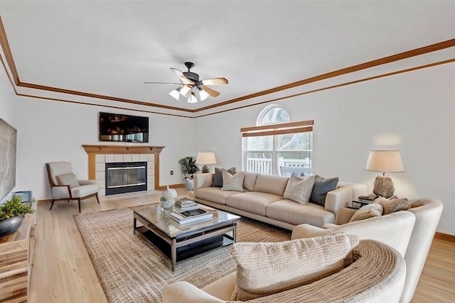 living room featuring a fireplace, hardwood / wood-style floors, ceiling fan, and crown molding