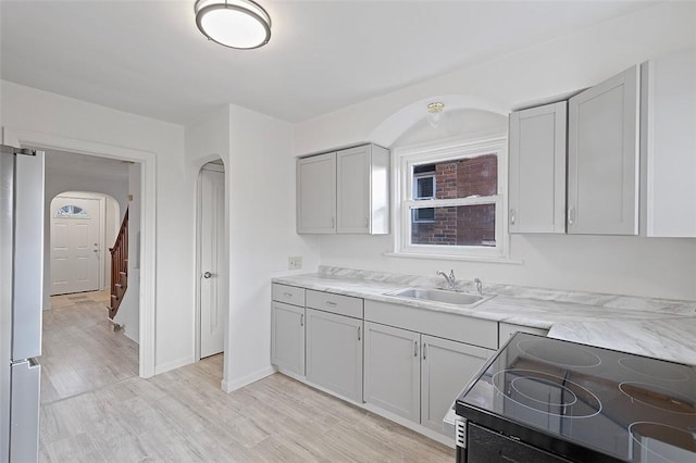 kitchen featuring stove, sink, gray cabinets, stainless steel fridge, and light wood-type flooring