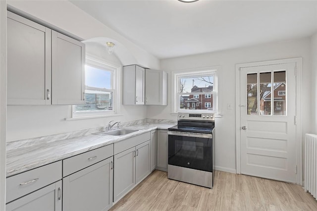 kitchen with gray cabinetry, radiator, sink, light hardwood / wood-style floors, and stainless steel range with electric stovetop