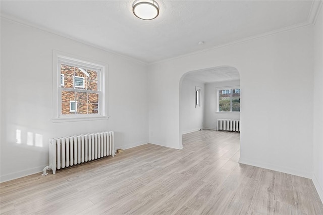 empty room with radiator heating unit, light wood-type flooring, and crown molding