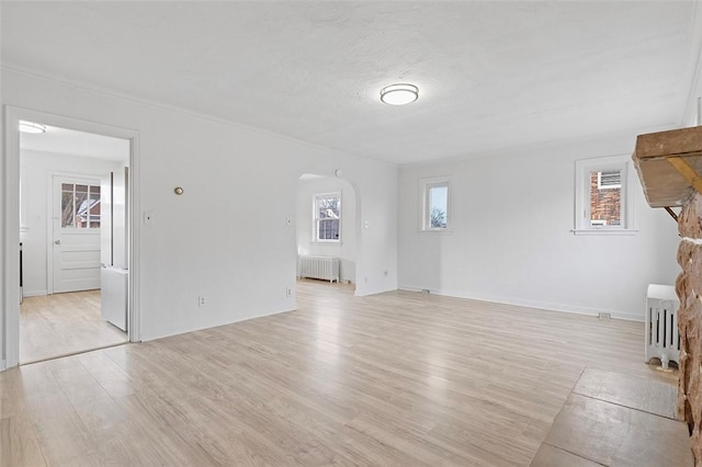 unfurnished living room featuring radiator, a healthy amount of sunlight, and light wood-type flooring