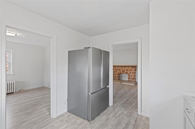 kitchen featuring radiator, stainless steel fridge, a stone fireplace, and light wood-type flooring