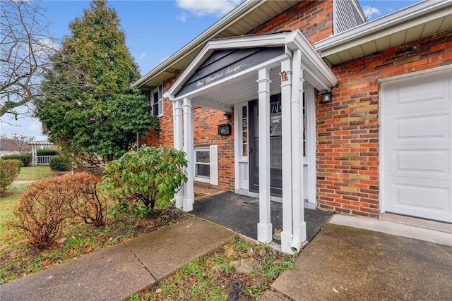 view of exterior entry featuring a garage and brick siding