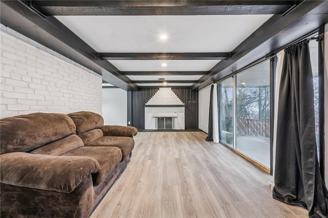 living room featuring beam ceiling, light hardwood / wood-style flooring, brick wall, and a brick fireplace