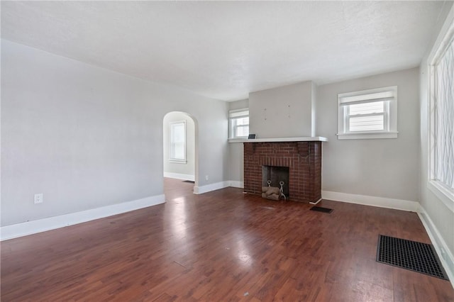 unfurnished living room with dark wood-type flooring and a brick fireplace