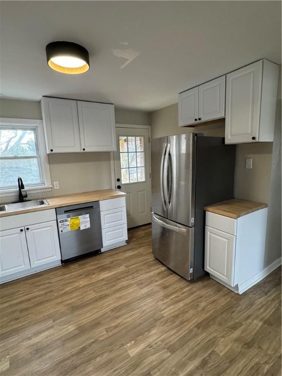 kitchen with sink, wooden counters, appliances with stainless steel finishes, white cabinets, and light wood-type flooring