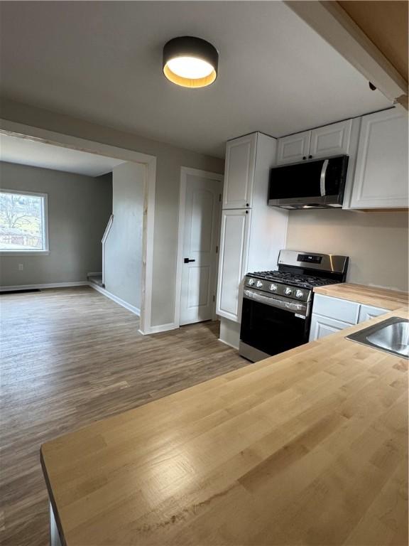 kitchen featuring white cabinets, stainless steel appliances, light wood-type flooring, and wood counters