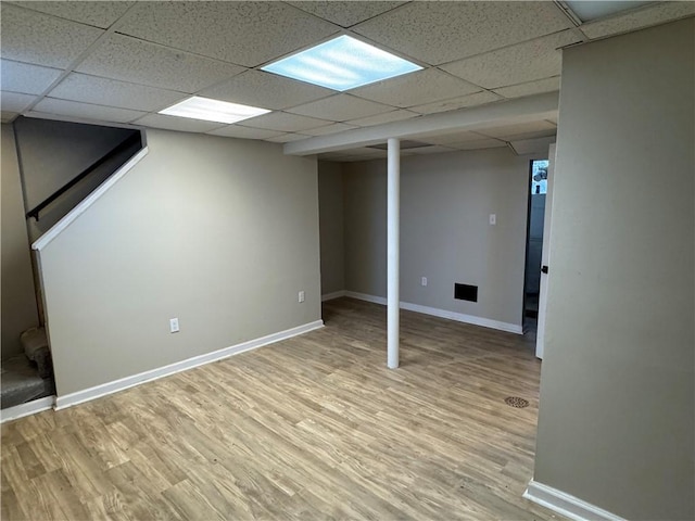 basement featuring a paneled ceiling and light hardwood / wood-style floors