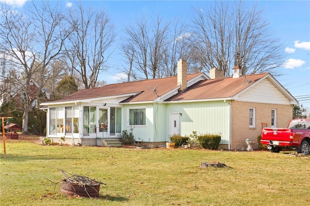 back of house featuring a lawn, an outdoor fire pit, and a sunroom