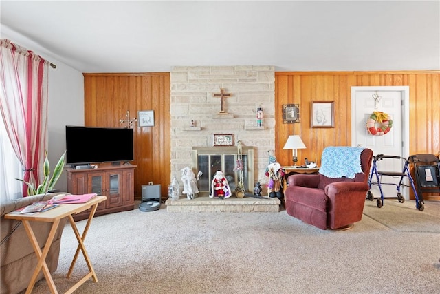 carpeted living room with a stone fireplace and wood walls