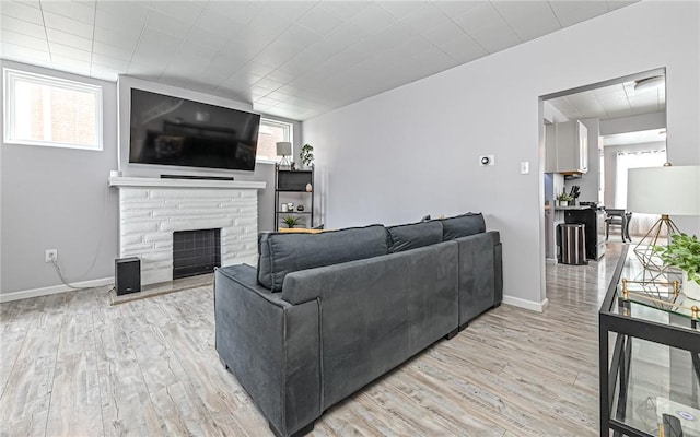 living room with light hardwood / wood-style floors, a stone fireplace, and plenty of natural light