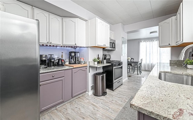 kitchen featuring white cabinets, stainless steel appliances, light stone counters, and sink