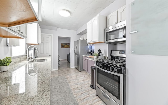 kitchen with light stone counters, stainless steel appliances, sink, white cabinets, and light hardwood / wood-style floors