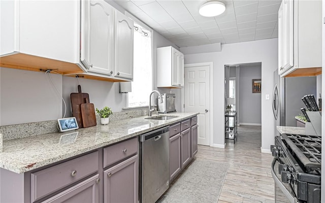 kitchen with light stone countertops, stainless steel dishwasher, black gas range oven, sink, and white cabinets