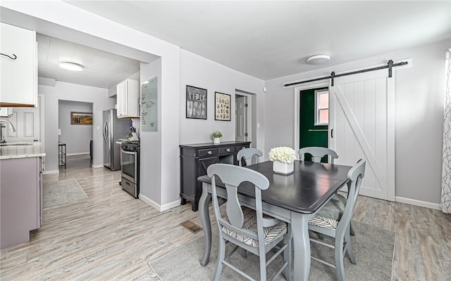 dining space with a barn door, sink, and light hardwood / wood-style flooring