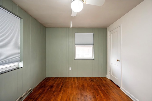 unfurnished room with dark hardwood / wood-style flooring, ceiling fan, and wooden walls