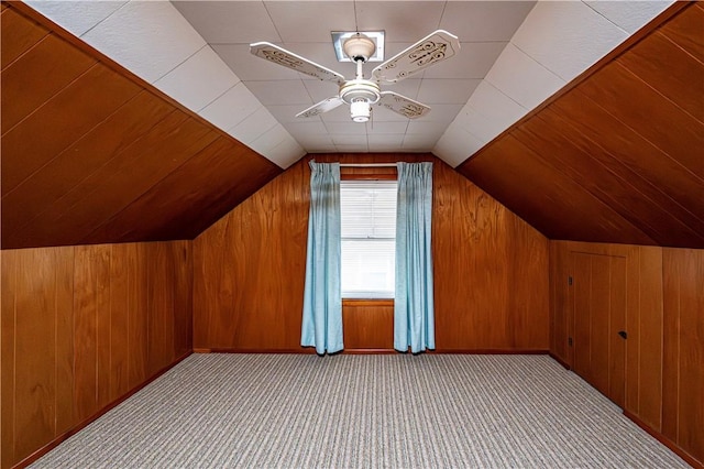 bonus room featuring light colored carpet, vaulted ceiling, ceiling fan, and wooden walls