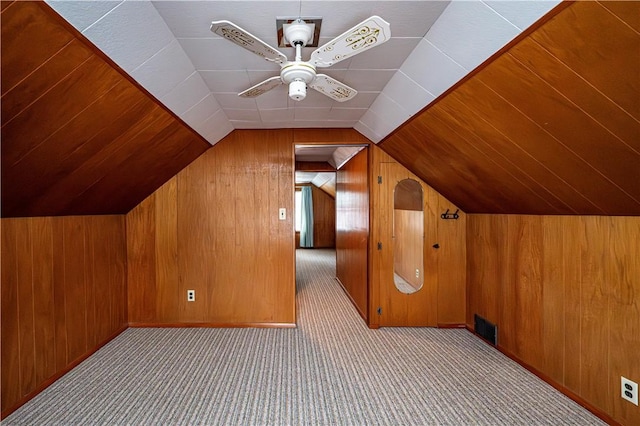 additional living space featuring ceiling fan, wood walls, light colored carpet, and vaulted ceiling