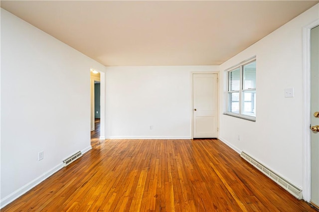 empty room featuring baseboard heating and hardwood / wood-style floors