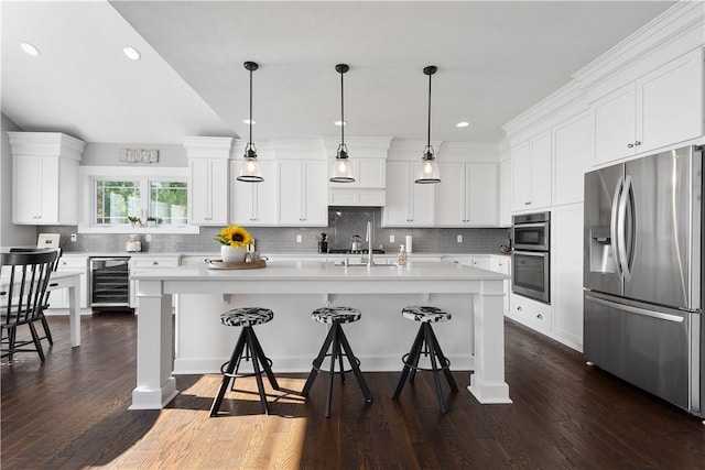 kitchen featuring a center island with sink, white cabinets, stainless steel appliances, and decorative light fixtures