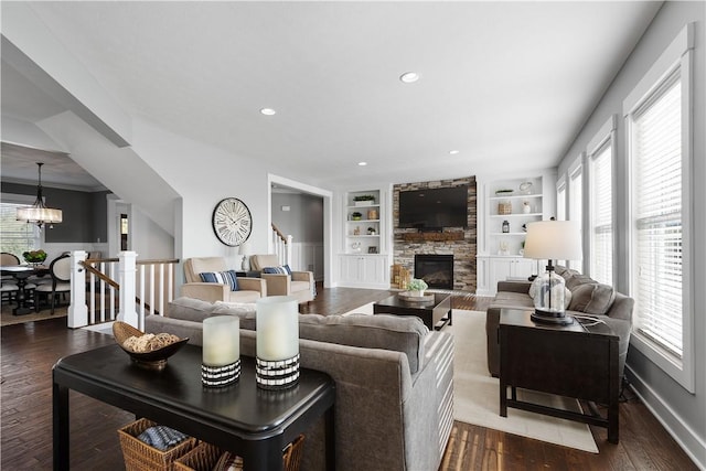 living room with a fireplace, built in shelves, an inviting chandelier, and wood-type flooring