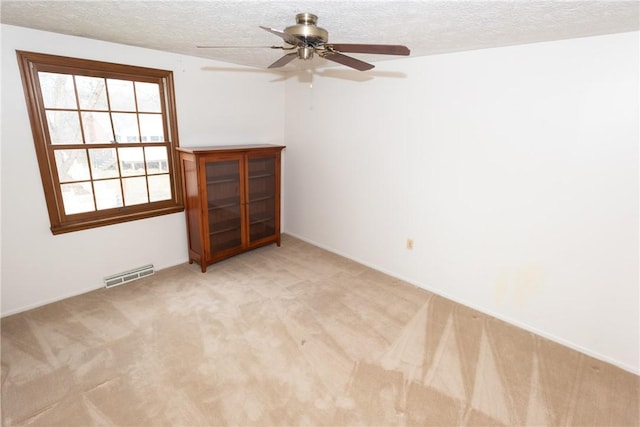 unfurnished room featuring ceiling fan, light colored carpet, and a textured ceiling