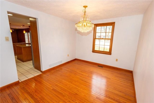 empty room featuring a chandelier, a textured ceiling, and light wood-type flooring