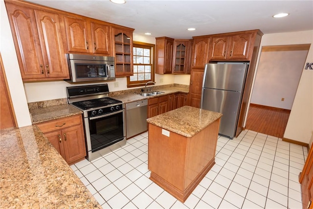 kitchen with stainless steel appliances, light stone counters, a kitchen island, and sink