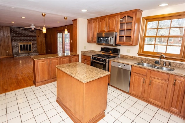 kitchen with sink, hanging light fixtures, a brick fireplace, a kitchen island, and appliances with stainless steel finishes