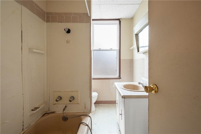 bathroom featuring vanity, toilet, tile walls, and a bathing tub