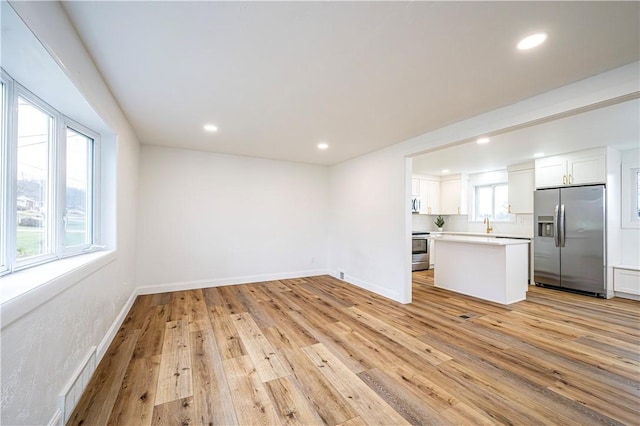 kitchen featuring light wood-type flooring, stainless steel appliances, white cabinetry, and a wealth of natural light