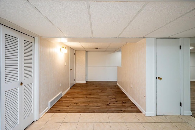 basement with a paneled ceiling, wooden walls, and light tile patterned floors