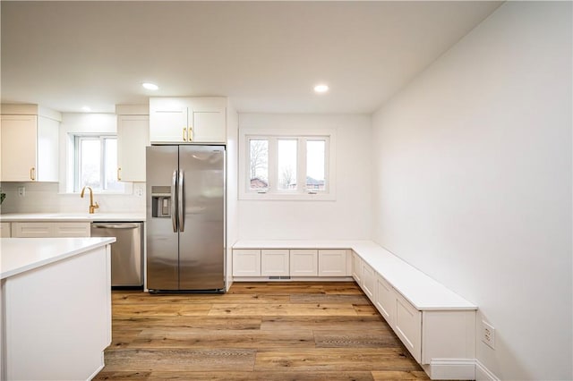 kitchen with a healthy amount of sunlight, white cabinetry, light hardwood / wood-style floors, and appliances with stainless steel finishes