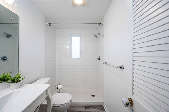 bathroom featuring toilet, wood-type flooring, and tiled shower