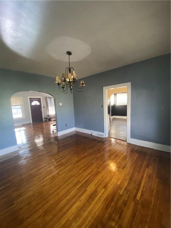 unfurnished room with dark hardwood / wood-style floors, a wealth of natural light, and a chandelier