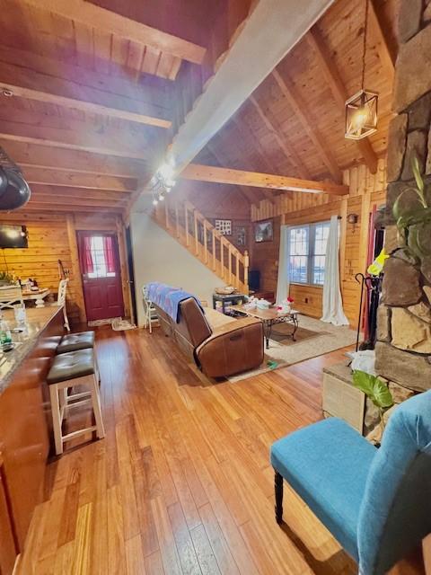 living room with vaulted ceiling with beams, wooden walls, light hardwood / wood-style flooring, and wooden ceiling