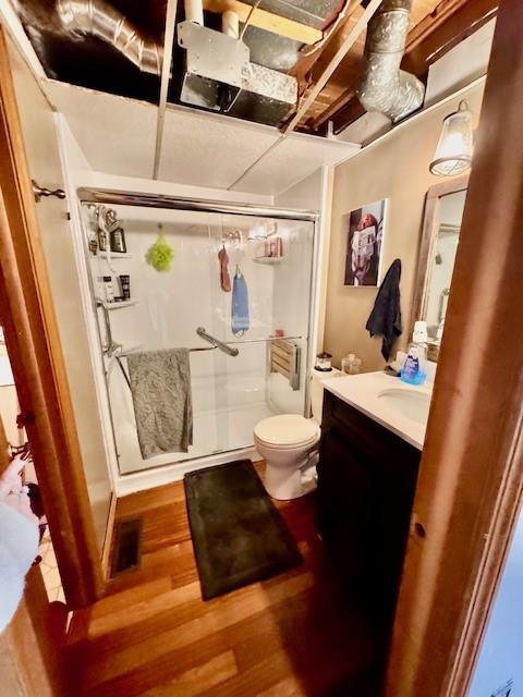 bathroom featuring vanity, wood-type flooring, a shower with shower door, and toilet