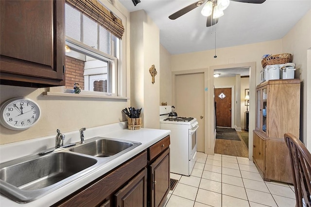 kitchen featuring white range with gas stovetop, sink, ceiling fan, light tile patterned flooring, and dark brown cabinetry