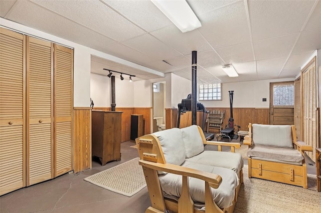 sitting room with concrete floors, a drop ceiling, and wooden walls