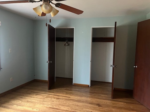 unfurnished bedroom featuring ceiling fan, hardwood / wood-style floors, and two closets