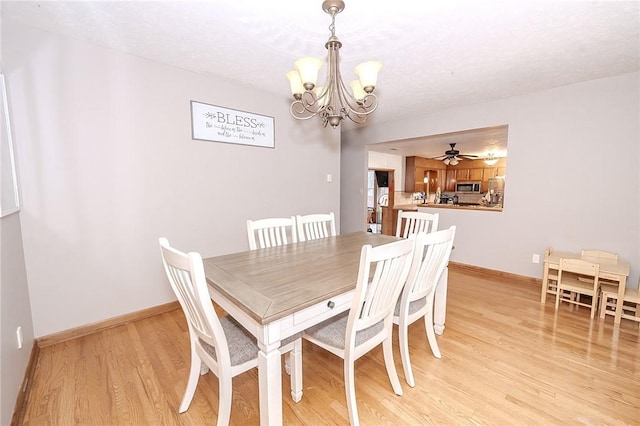 dining space with ceiling fan with notable chandelier and light hardwood / wood-style flooring