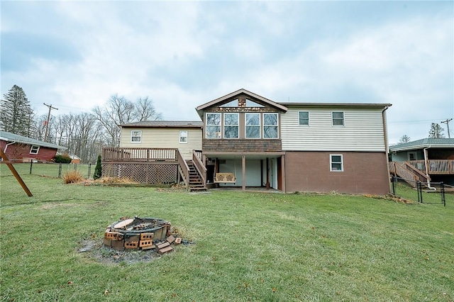 back of property with a fire pit, a wooden deck, and a lawn