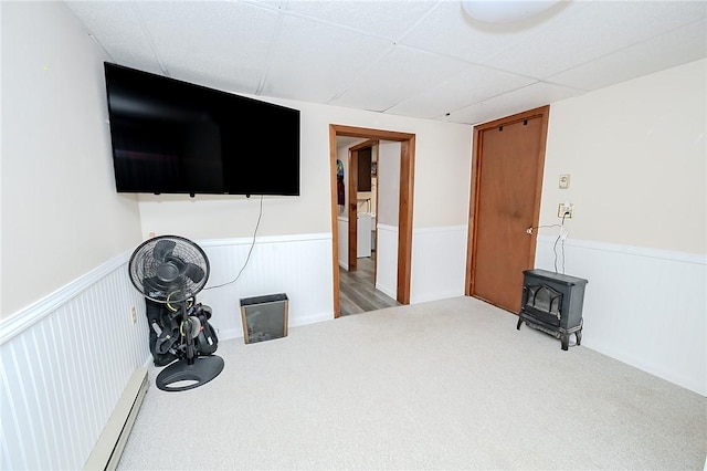 interior space featuring a drop ceiling, carpet floors, washer / clothes dryer, and a wood stove