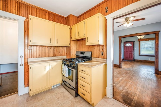 kitchen featuring ceiling fan, wood walls, and stainless steel range with gas stovetop