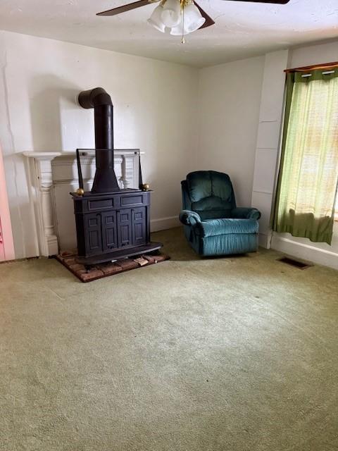 sitting room with carpet flooring, ceiling fan, and a wood stove